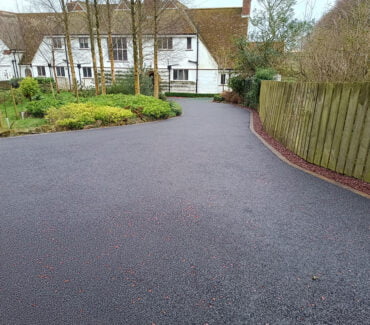 A tarmac driveway featuring a classic black surface with red pre coated chip accents, meticulously installed by W Miller & Sons in Lesbury, Alnwick, Northumberland